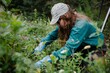 A volunteer kneels in a field of flowers, removing invasive species to restore native plant communities and improve the ecosystem