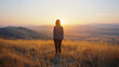 A tranquil scene of a woman on a hilltop at dawn with back button focus accentuating the gentle yellows and soft grays of early morning