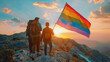 Friends on a mountain hike celebrating gay pride with a rainbow flag unfurled against the backdrop of a stunning sunset