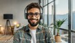 © Marko - Portrait of an attractive young bearded hipster man smiling at the camera, wearing headphones, standing in the modern house, wearing a casual shirt. The view while the video-calling concept