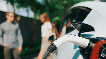 Wall Mural - Focused EV electric car charging in green sustainable city outdoor garden in summer show lifestyle on blur background of young couple in urban green sustainable rechargeable electric vehicle innards