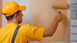 © DenisProduction.com - Builder paints white wall in beige color with a roller. Professional wall painting.