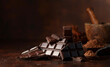 Broken dark chocolate bar and cocoa powder on a brown table.
