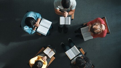 Wall Mural - Time lapse of skilled diverse prayer clasping hand and praying to god while sitting at chair in circle. Top down aerial view of people folded hand while sitting with opened bible on laps. Symposium.