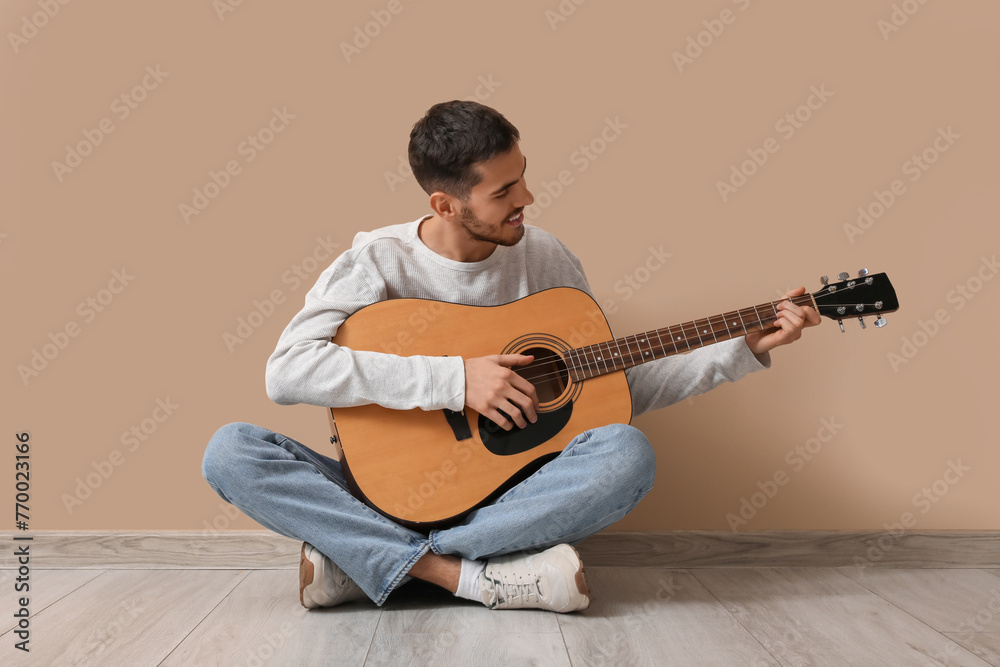 Handsome young man playing guitar on beige background