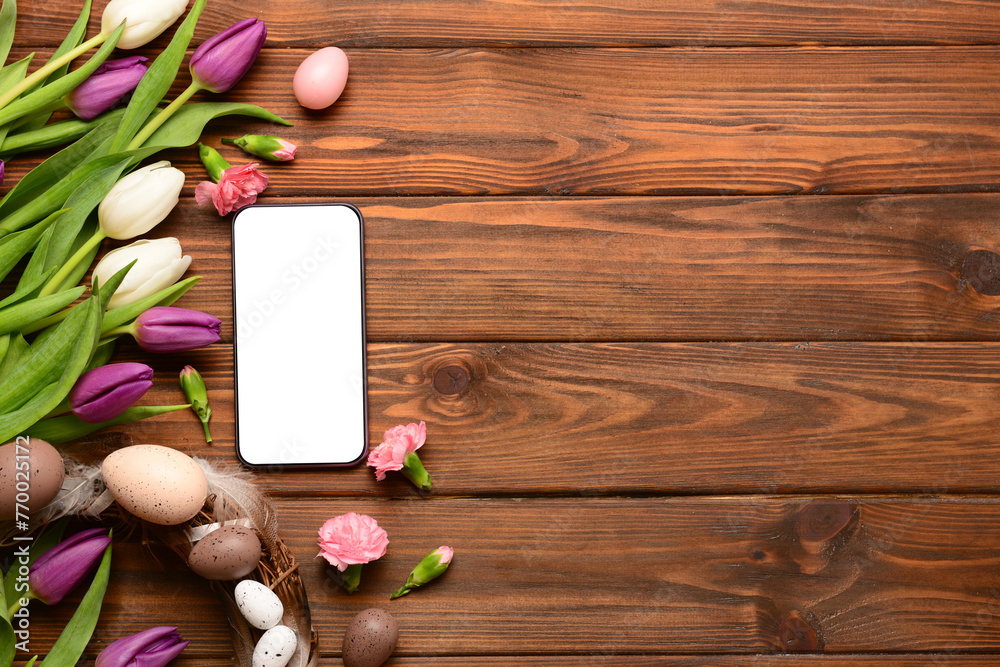 Composition with modern mobile phone, beautiful flowers and Easter wreath on wooden background