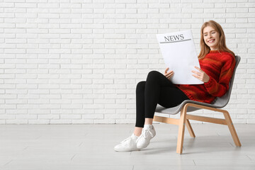 Wall Mural - Young woman reading newspaper while sitting on chair near white brick wall