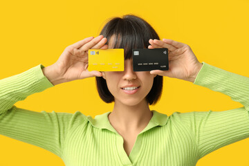 Beautiful young woman with credit cards on yellow background