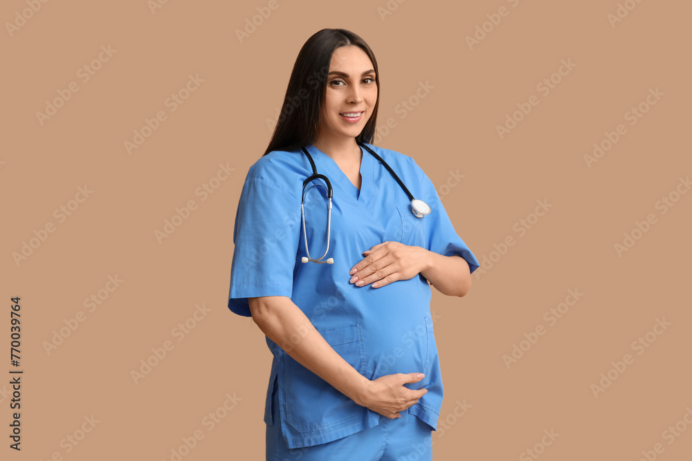 Beautiful young pregnant doctor with stethoscope on brown background