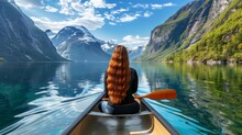  A Woman With Long, Red Hair Paddles A Canoe On A Lake Before Snow-capped Mountains