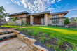 High noon captures a contemporary home exterior with vibrant green grass, brick, and stacked stone walls amidst detailed landscaping, inviting under the bright midday sun.