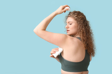 Poster - Beautiful young woman applying deodorant on blue background