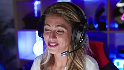 Sticker - Confident young blonde streamer woman gleefully gaming, engaged in a video call in her dark home gaming room. she's happily streaming, fully immersed in the virtual world of technology