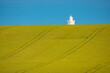 The white lighthouse tower peeks over the top of a rolling golden wheat field