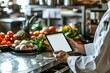 © ChaoticMind - Professional chef in a modern kitchen holding a tablet with a blank screen, surrounded by fresh ingredients