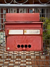 Vintage Red Mailbox Mounted On A Metal Gate With A Tiled Floor Background, Showcasing Retro Communication Methods.
