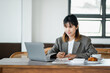 © Satori Studio - Businesswoman is diligently working on her laptop, writing notes at a cafe, accompanied by a fresh cup of coffee and pastry.