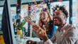 © Alina Tymofieieva - Happy guy in an office environment, sitting in front of a computer blowing confetti on his female colleague
