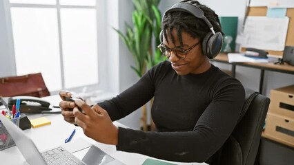 Sticker - Focused african woman with dreadlocks working in office using headphones and smartphone.