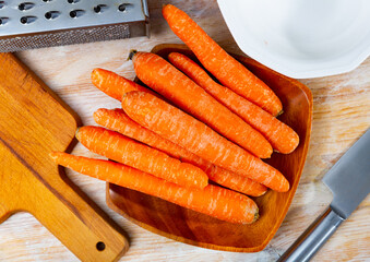 Wall Mural - Pile of fresh raw carrots on wooden plate. Food ingredient.