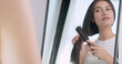 Beautiful young woman combs her hair while standing in front of the mirror at home.