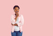 Happy laughing curly young afroamerican girl in pink shirt and jeans thinking looking aside up on copy space on pink background. Banner for advertisement, marketing with cute african american girl.