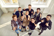 © Studio Romantic - Happy business team giving thumbs up all together. Cheerful young people standing in office, looking up, showing like gestures and smiling. High angle view, shot from above. Success concept