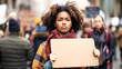 Young african woman holding a cardboard sign at street, surrounded by a crowd of people, during a peaceful protest for human rights. space for copy text or a message on the board
