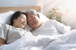 An elderly Asian man and woman laying together in bed, showcasing love and companionship