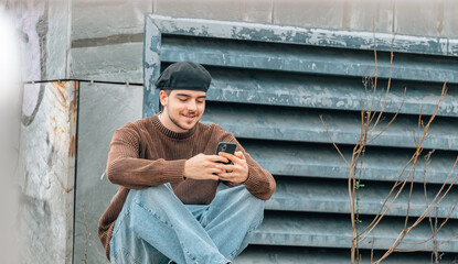 Poster - young man sitting on the street with mobile phone chatting or playing online