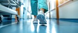 Fototapeta Kosmos - Doctor walks along the corridor of the clinic. Hospital background. Medical healthcare concept. Med office. Nurse rushes to help a patient. Ground level view. Legs close up.