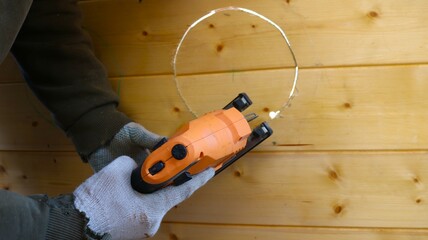 working with a jigsaw on a wooden surface, cutting a circle with a jigsaw, a working construction tool in male hands in gloves close-up during decorative woodworking