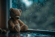 Teddy bear sitting beside the window while raining