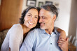 © peopleimages.com - Mature couple, happy and hug in home for portrait with bonding, care and together with love in living room. Senior people, man and woman with embrace, marriage and holding hands for support in lounge