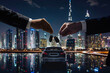 Two formally dressed people exchanging car keys against dazzling cityscape and waterfront reflecting lights