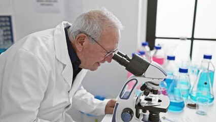 Wall Mural - Smiling senior man scientist confidently using microscope in laboratory, joyfully immersed in scientific research and discovery