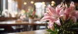 Fototapeta  - A beautiful bouquet of pink lilies, a type of flowering plant, is elegantly displayed on a wooden table in a cozy restaurant setting