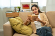 © Chanakon - Asian beautiful woman sitting reading book on cozey couch sofa in living room with sun light morning. People female stay home part time relax at home.