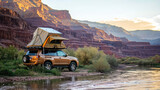 Fototapeta  - An SUV with a tent on the roof stands on the river bank against the backdrop of a mountainous landscape, embodying the spirit of travel. Offroad travel