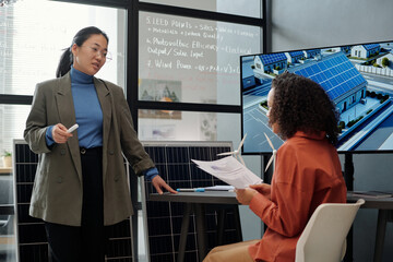 Aufkleber - Young Asian businesswoman in formalwear discussing points of new natural energy project with colleague while preparing for presentation