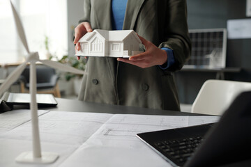 Aufkleber - Model of house held by young unrecognizable female architect in formalwear standing by workplace with blueprints and laptop