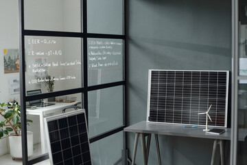 Poster - Grey desk with models of solar panel and windmill standing by wall of spacious modern office with workplaces of architects and designers