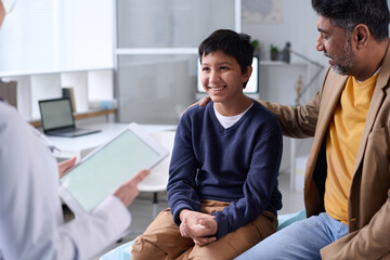 Portrait of smiling Middle Eastern boy visiting doctor in clinic with father supporting