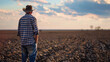 A farmer looking over a parched field once fertile now unyielding due to unpredictable weather patterns.