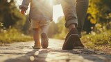 Fototapeta Kosmos - Little boy hold his father hand. Son and dad walk together in park. Happy family concept. Fatherhood. Daddy care baby. Summer stroll at nature. Ground level back view. Fun carefree vacation.