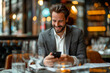 Smiling businessman in a grey suit sitting in a cafe, engrossed in his mobile phone amidst ambient lighting.