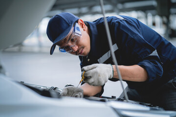 Wall Mural - A mechanic is working on a car engine, wearing a blue shirt and a blue hat. He is wearing gloves and goggles, and has a wrench in his hand