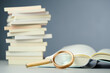 © patpitchaya - Magnifying glass on an opened book with a books pile and copy space in the background, searching information, glossary