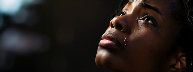 Young black woman looking up praying to God with tears in eyes, being touched by His Grace. Christian and faith concept.