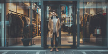 Man In Camel Coat Standing In Front Of A Clothing Store.